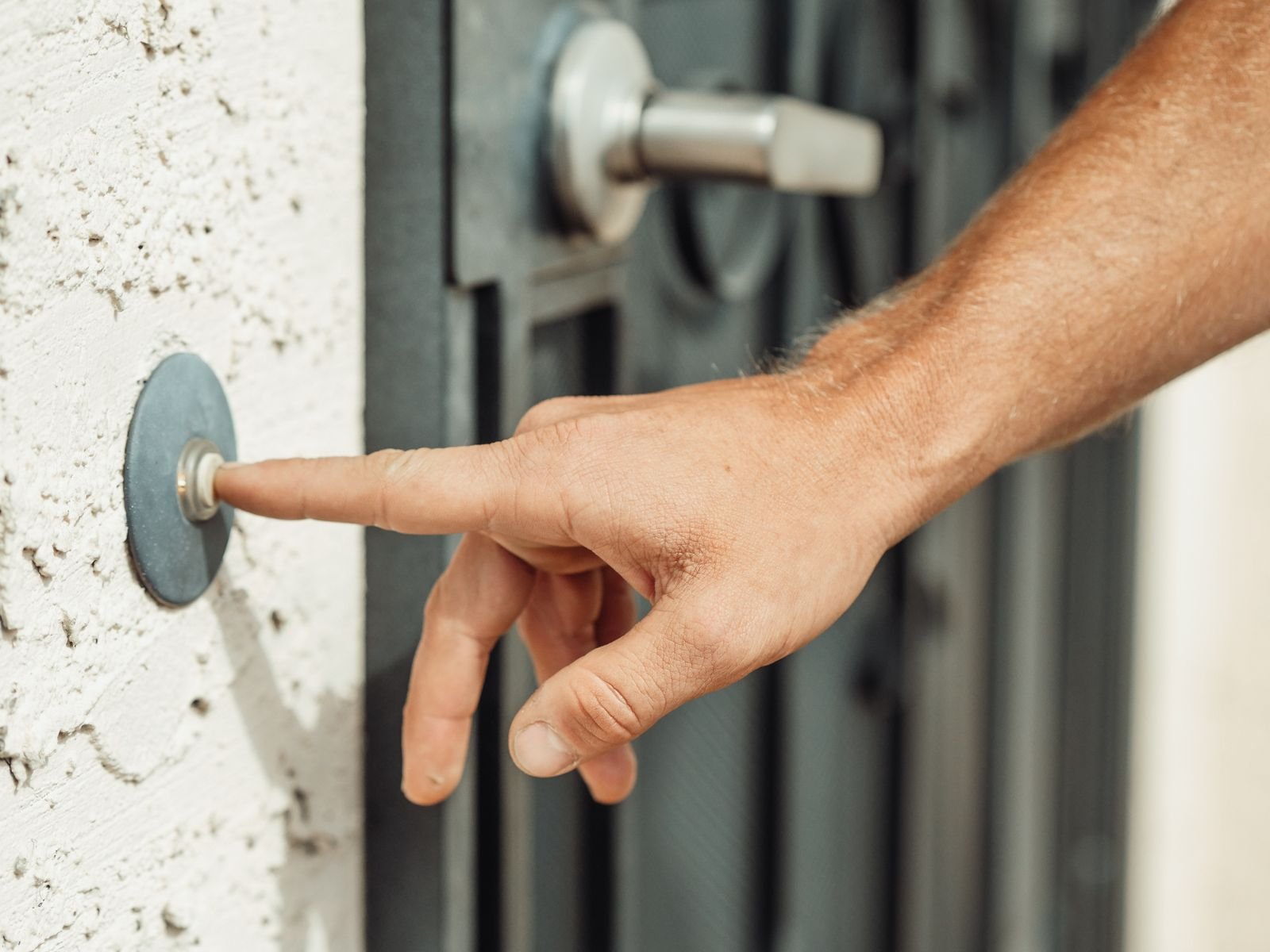Finger pressing a video doorbell button on a front door